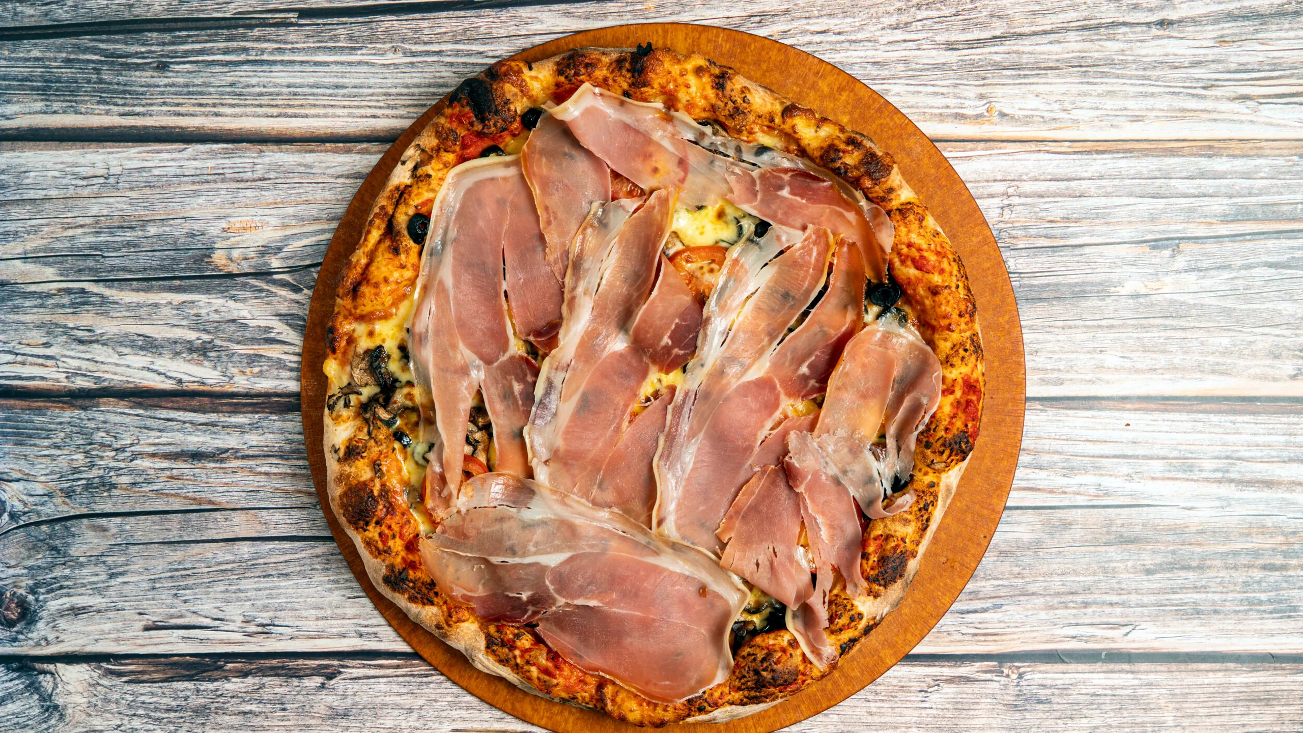 Pizza topped with prosciutto on a wooden table
